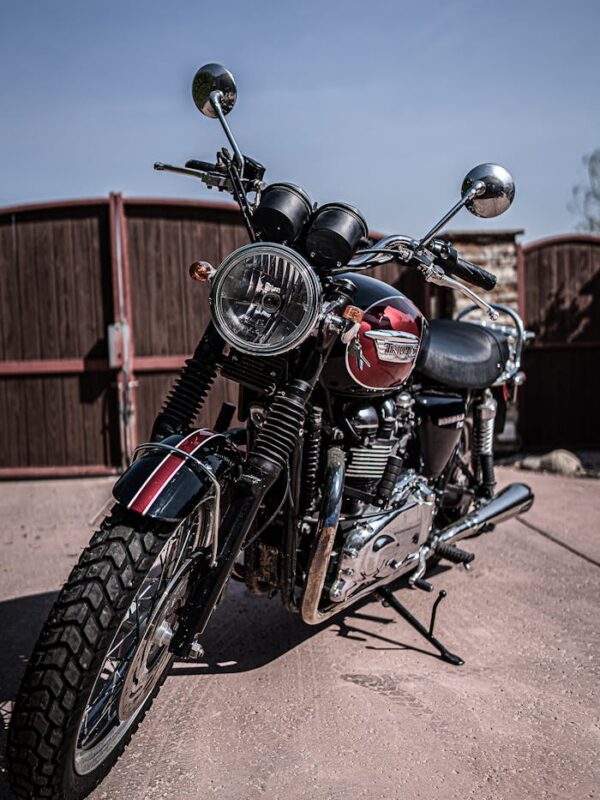 Black and red retro motorcycle with chrome details parked on asphalt road against cloudless blue sky
